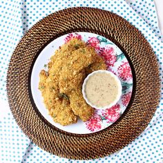 a plate topped with fried food next to a bowl of dipping sauce on top of a blue and white table cloth