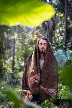 a man wrapped in a blanket standing in the woods