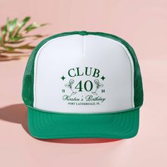 a green and white trucker hat sitting on top of a pink surface