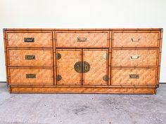 an old bamboo dresser with four drawers and two doors on each side, in front of a white wall