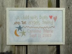 a cross stitched sign hanging on the side of a wooden fence that says, a child was born and the angels smiled