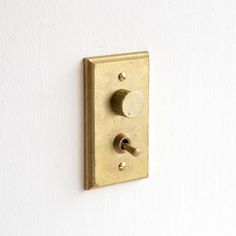 a wall mounted light switch on the side of a white wall with two black knobs