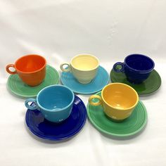 six cups and saucers are arranged on the same placemat, each with different colors