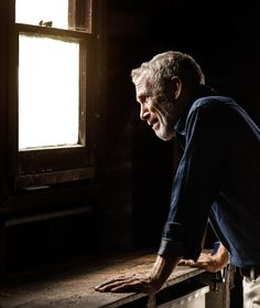 an older man leaning on a window sill with his hand on the ledge in front of him