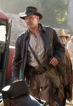 a man in a hat and leather jacket standing next to a truck with other men