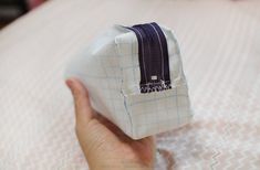 a hand is holding a small bag on top of a bed with white and blue checkered sheets