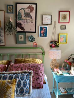 a bed with many pillows and pictures on the wall above it, along with a small table