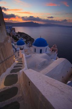 the sun is setting over an ocean and some white buildings with blue domes on them