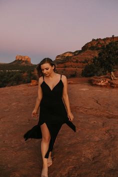 a woman in a black dress walking across a desert