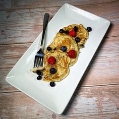 two pancakes with berries and blueberries are on a white plate next to a fork