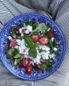 a blue and white plate filled with strawberries and spinach salad on top of a striped cloth