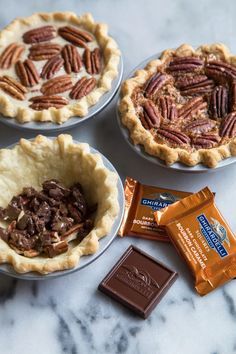 three pies with pecans, chocolate and candy bars on the counter top next to them