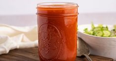 a glass jar filled with sauce next to a bowl of lettuce