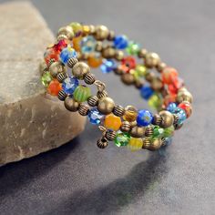 two bracelets with multi colored beads are sitting on a rock