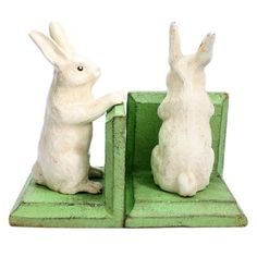 two white rabbits are standing on their hind legs in front of a green bookend