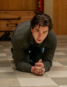 a man in black shirt laying on checkered floor next to wooden cabinet and dresser