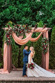 a bride and groom standing under an outdoor wedding ceremony arch with pink draping