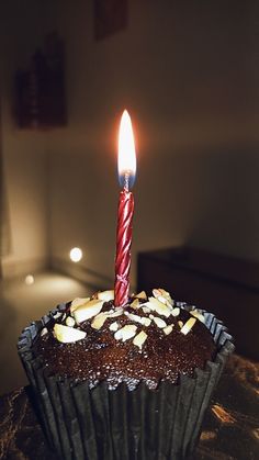 a chocolate cupcake with a single lit candle on it's top, sitting on a table