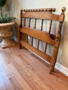 a wooden bed frame sitting on top of a hard wood floor next to a potted plant