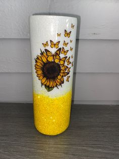 a yellow and white cup with butterflies on it sitting on top of a wooden table