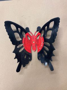 a black and red butterfly shaped clock on the wall with tags attached to it's wings