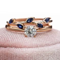 two gold rings with blue and white stones on top of a pink velvet cushioned surface