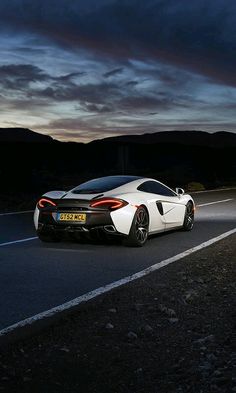 a white sports car driving down the road at night with dark clouds in the background