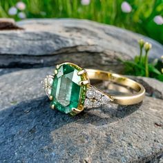 an emerald and diamond ring sitting on top of a rock