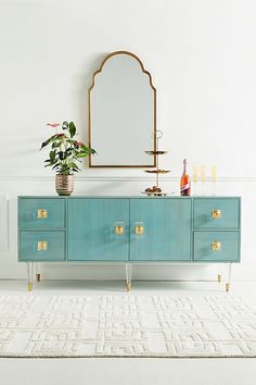 a blue dresser with a mirror and vase on it in a room that has white walls