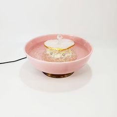 a pink bowl sitting on top of a white table next to a black corded light