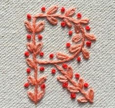 an embroidered letter with red beads and leaves