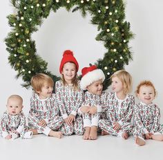 a group of children wearing christmas pajamas and santa hats sitting in front of a wreath