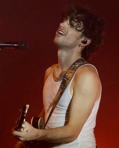 a man holding a guitar in his right hand and singing into a microphone on stage