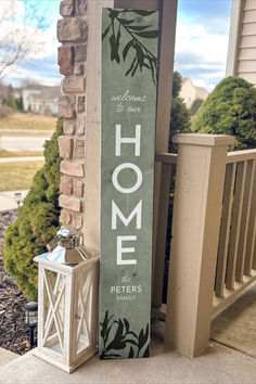 a sign that says home on it next to a porch with a lantern and potted plant