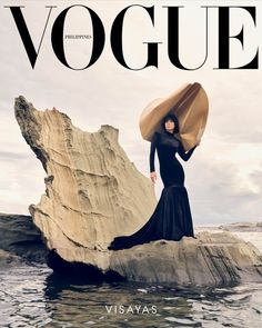 a woman standing on top of a rock next to the ocean wearing a long black dress