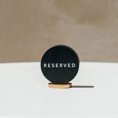 a round black object sitting on top of a white table with the word reserved printed on it