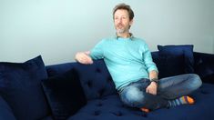 a man sitting on top of a blue couch with his legs spread out and one foot in the air