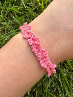 a pink crochet bracelet on someone's arm in the grass with green grass behind it