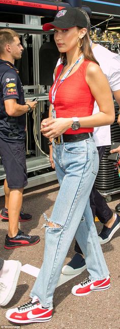 a woman in red shirt and jeans walking on street next to man wearing black hat