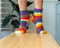 a woman's legs with colorful socks on top of a wooden table next to a potted plant