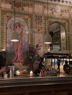 a woman standing behind a bar in front of a wall with paintings on the walls