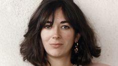 a close up of a person with long hair and wearing a pink shirt against a white wall