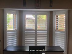 an empty room with white shutters on the windows and a table in front of it