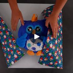 a person holding an owl stuffed animal on top of a box with wrapping paper around it