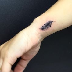 a person's arm with a small black feather tattoo on the left forearm and wrist