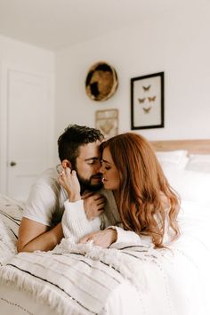 a man and woman laying on a bed with white sheets looking at each other's eyes