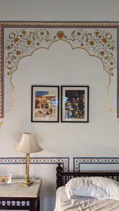 two pictures on the wall above a bed in a room with white walls and gold trim