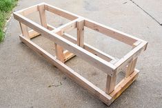 a wooden planter sitting on top of a cement floor next to grass and a sidewalk