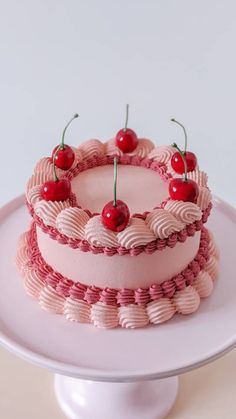 a cake with pink icing and cherries sitting on top of a white plate