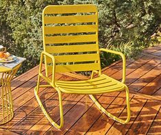 a yellow rocking chair sitting on top of a wooden deck next to a small table